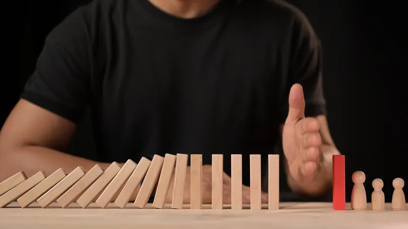 Hand about to stop falling dominoes lined up on a table.