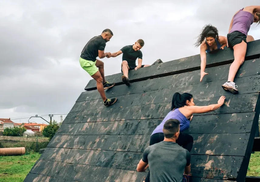 People climbing a steep obstacle wall during an outdoor challenge.
