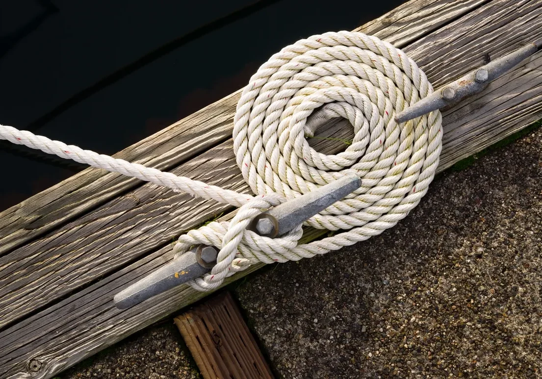 Coiled white rope with a metal hook on a wooden dock.